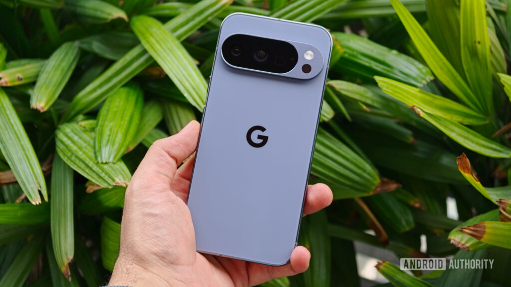 A hand holding the Google Pixel 10 Pro, showcasing the prominent horizontal camera visor against a lush green leafy background